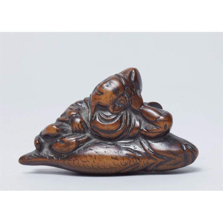 A boxwood netsuke of Ebisu lying on a sea bream. 18th century