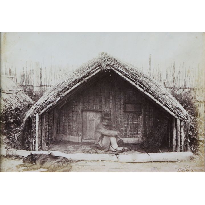 PHOTOGAPHER UNKNOWN [Burton Bros attrib] - View of a Māori man sitting in the porch of a whare [or reed house]